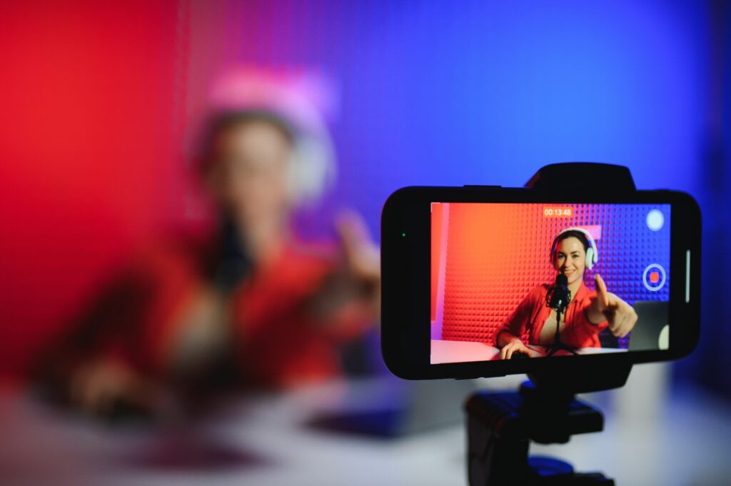 Positive trendy blogger woman speaking at smartphone webcam on tripod, recording post for vlog